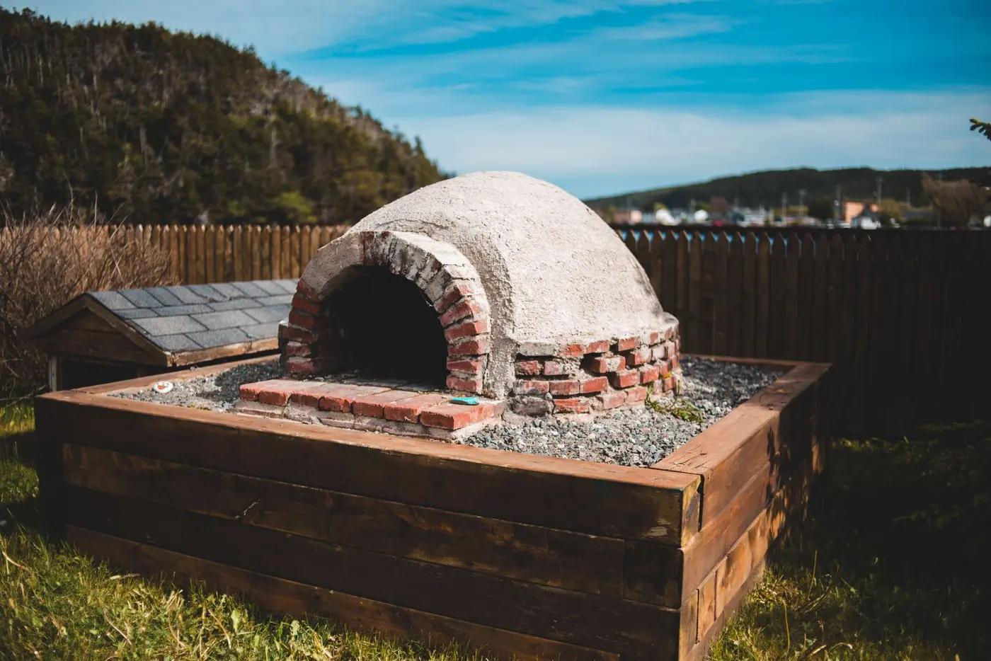 A brick outdoor oven built in place beside a timber fence