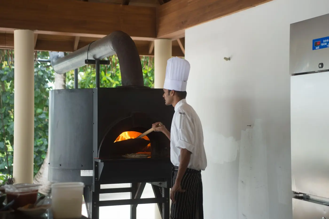 A chef in whites working at a commercial wood-fired oven