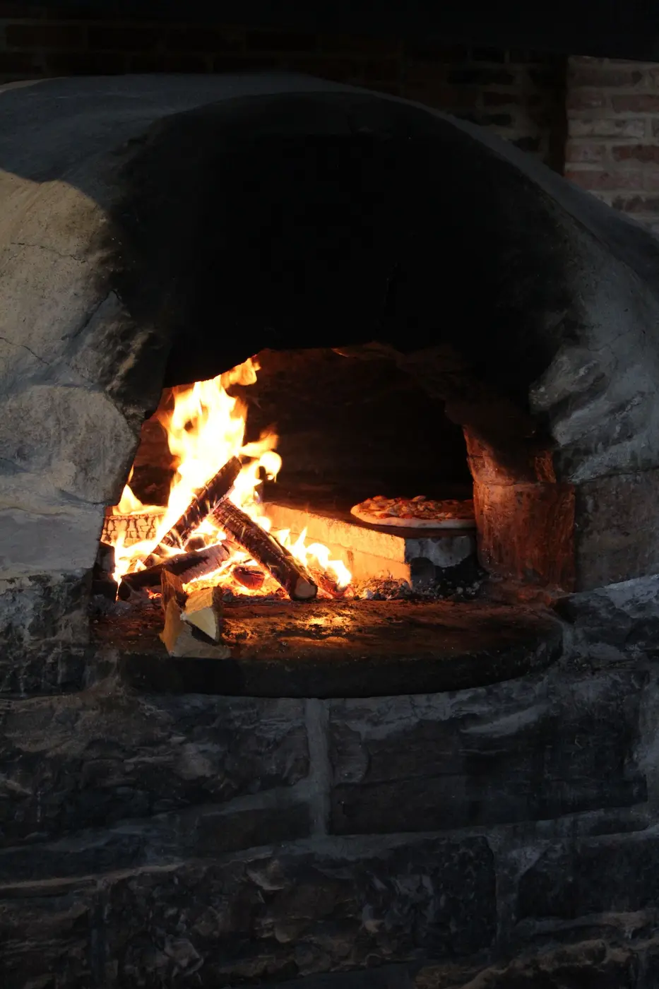 Firewood burning down to embers inside a brick oven
