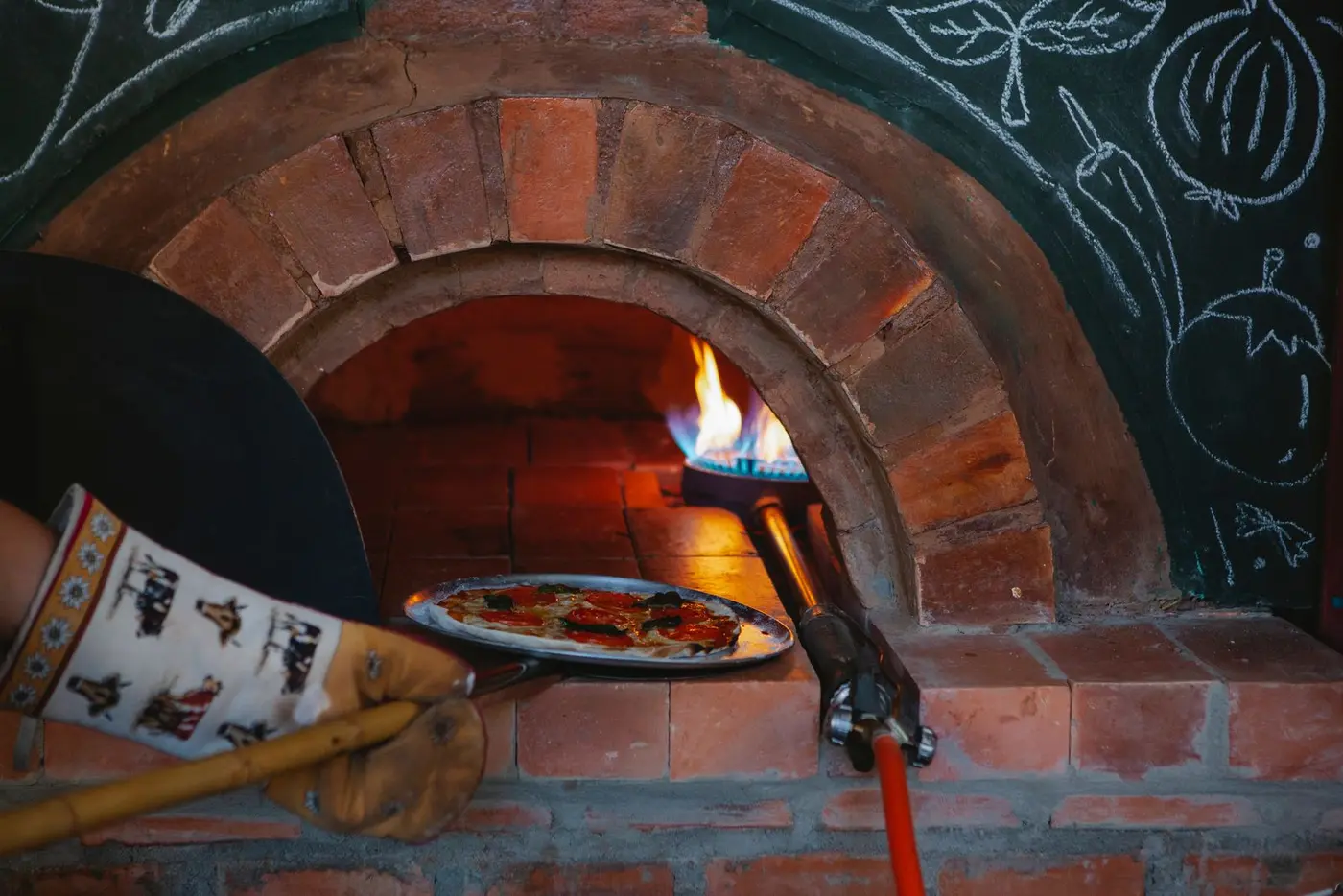 A chef sliding a pizza into a wood-fired oven during service