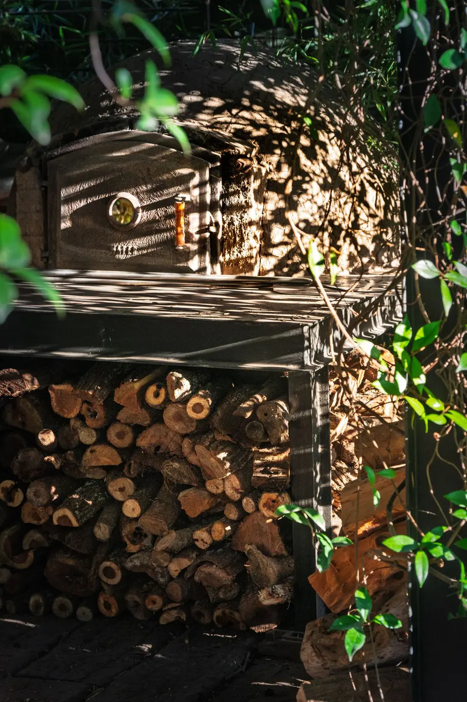 A rustic outdoor wood-fired oven with logs stacked beneath